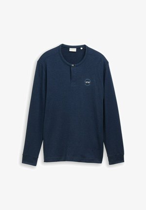 Chemise henley à manches longues bleu marine avec un bouton près du col rond et un petit texte imprimé circulaire sur la poitrine gauche.