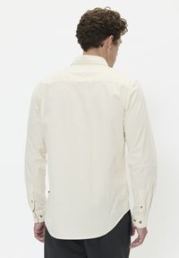 Camicia a maniche lunghe color beige chiaro con colletto botton-down, polsini a due bottoni e orlo curvo. Tessuto morbido con un design semplice.