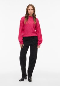 Jasnoróżowy, oversize'owy sweter z długimi rękawami, zestawiony z czarnymi, szerokimi spodniami i czarnymi, skórzanymi botkami na obcasie. Sweter w jednolitym kolorze, o fakturowanym dzianiu.