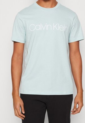 T-shirt en coton bleu clair avec col rond et manches courtes, arborant le logo "Calvin Klein" imprimé en blanc sur le devant.