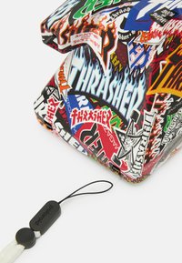 Tasche mit einer glänzenden Oberfläche, die mit verschiedenen bunten Logos und Grafiken bedeckt ist, einschließlich Flammen und einem schwarzen Zugbandanhänger.