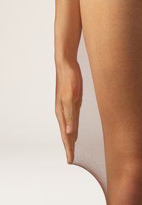 Collant trasparente color carne si adagia su una mano, evidenziando una superficie liscia. Il materiale sembra leggero e semi-trasparente, rivelando la pelle sottostante.