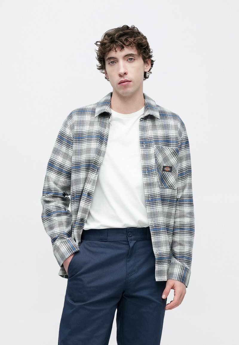 Kariertes Hemd in Grau und Blau aus Flanell, mit Kragen, Brusttasche und durchgehender Knopfleiste. Kombiniert mit marineblauen Hosen.
