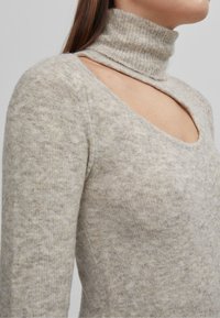Pull à col montant gris clair avec une découpe sur le haut de la poitrine, fabriqué en tissu en maille douce avec une finition texturée.