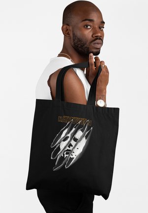Zwarte tote bag met een gestileerd wit gezicht en krassporen, met daarboven in het geel "John Carpenter's Halloween" gedrukt.