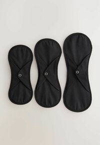 Trzy czarne materiałowe podpaski menstruacyjne o różnych rozmiarach, z centralnym zapięciem na zatrzask i konturowym kształtem. Miękka tekstura, gładkie krawędzie.