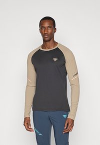 Hosszú ujjú sportpóló fekete testtel, bézs ragl�án ujjakkal és logóval a mellkason. Stretch anyaggal készült, a kényelem és a mozgásszabadság érdekében.