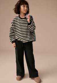 Sweatshirt à rayures noires et blanches, coupe décontractée ; associé à un pantalon large noir et des chaussures marron à enfiler ; veste en jean sur l'épaule.