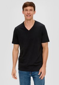 T-shirt nera a maniche corte con scollo a V realizzata in cotone, con una texture morbida e una vestibilità regolare, abbinata a jeans in denim blu.
