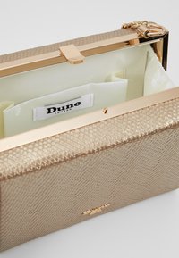 Portafoglio rettangolare in materiale metallico dorato testurizzato. Presenta una struttura e una chiusura in tonalità dorata, con un interno in morbido tessuto e un'etichetta con logo.