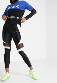 Leggings atléticos negros con cortes de malla, acentuados con detalles en blanco y rojo. Combinados con una camiseta gráfica azul y negra. Zapatillas verde neón.