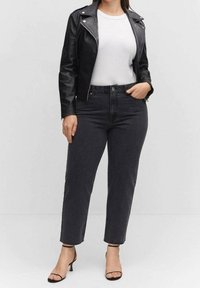 Chaqueta de cuero negra estilo motorista sobre una camiseta blanca, combinada con jeans de mezclilla oscuros y tacones negros con tiras. Diseño sencillo con acentos mínimos.