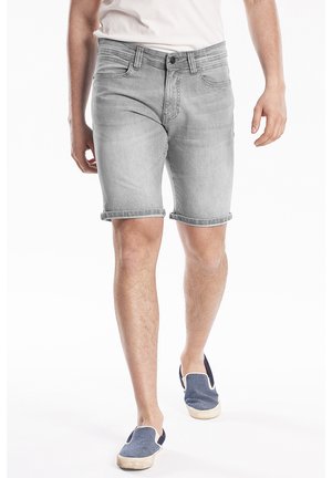 Shorts en denim gris au design ajusté, avec ourlets roulés, style à cinq poches, portés avec une chemise de couleur claire et des chaussures slip-on marines.