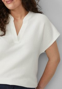 Witte, gestructureerde top met korte mouwen en een V-hals, vervaardigd uit ribstof en met een relaxte pasvorm, geschikt voor casual dragen.