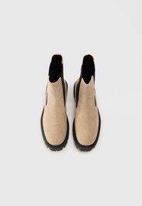 Beige semskede Chelsea-støvler med sorte elastiske sidet panels og en tekstureret sort gummisål. Rund tå-design med syede detaljer.