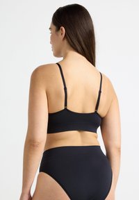 Bralette inalámbrico negro con tirantes ajustables; tela suave; diseño minimalista; combinado con ropa interior negra a juego de cintura alta.