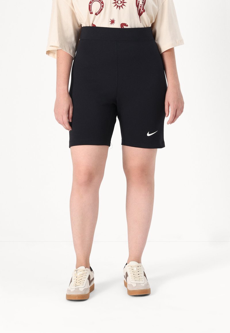 Zwarte sportshorts met een hoge taille, gemaakt van elastisch materiaal, met een wit Nike-logo op de onderste zoom. Gecombineerd met casual sneakers.