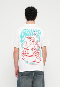 Bílé bavlněné tričko s barevným grafickým motivem na zádech, s modrým a červeným textem a kresleným ovocem v misce.