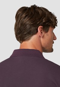 Polo shirt in diep paars met een gestructureerde stof. Kenmerkt zich door een klassieke kraag en een klein geborduurd logo op de achterkant.