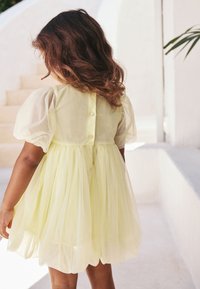 Kleid mit Puffärmeln aus weichem, gelbem Tüll, mit durchgehender Knopfleiste auf der Rückseite und ausgestellter Silhouette, in leichter, transparenter Textur.