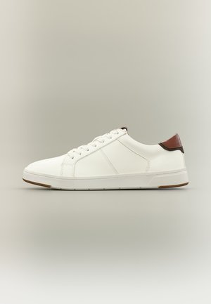 Weißer Sneaker mit niedrigem Schaft, weißen Schnürsenkeln, strukturierten Seitenpaneelen und braunem Fersenlasche vor neutralem Hintergrund.