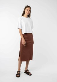 Korte, witte cropped t-shirt met korte mouwen, gecombineerd met een bruine rok tot de knie met een zijsplit. Zwarte sandalen met banden.