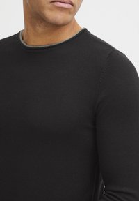 Svart langermet skjorte med ribbet tekstur og en kontrastfarge i grå rundt halsen. Tettsittende design med minimale sømdetaljer.