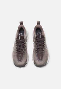Nike tenisice za trčanje s gornjim dijelom od sive i smeđe mreže, tamnim vezicama, podstavljenim okovratnikom, detaljima logotipa i teksturiranom gumenom potplatom. Lagani dizajn.