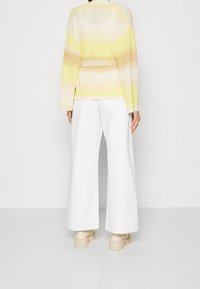 Suéter de manga larga con un degradado de amarillo a crema, con cintura ceñida y textura acanalada, combinado con pantalones anchos blancos.