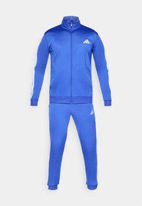 Modrý teplákový komplet z hladkej látky. Bunda má vysoký golier, plný zips a biele trojpásikové prvky. Nohavice majú elastický pás.