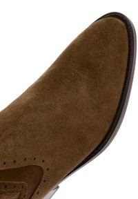 Brown suede men's dress shoe with brogue detailing and a pointed toe, photographed against a white background.