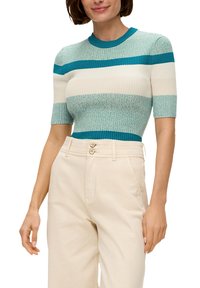 Kurzer, gestrickter Oberteil mit alternierenden Streifen in Teal, Creme und strukturierten Mustern. Kombiniert mit hochgeschnittenen Cremehosen.