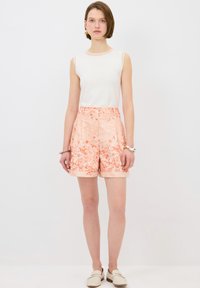 Haut sans manches léger en blanc associé à un short côtelé à motif floral pêche, avec une taille élastique et des ourlets retroussés.