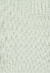 Detailní záběr bílé tkaniny s pleteným vzorem, která vykazuje texturovaný vzor s malými, rovnoměrně rozloženými smyčkami a mírně drsným povrchem.