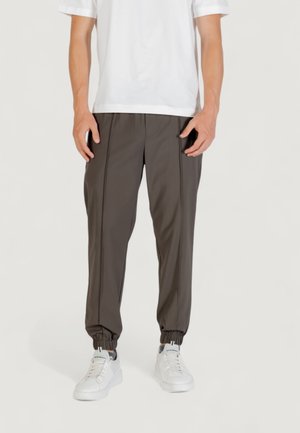 Pantaloni jogger grigio scuro con polsini elasticizzati, caratterizzati da due cuciture laterali e una texture liscia, abbinati a sneaker bianche e a una maglietta bianca semplice.