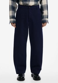 Námornícky modré nohavice s širokými nohavicami a hladkou textúrou, so zapínaním na gombík vpredu a bočnými vreckami, skombinované s károvanou košeľou.