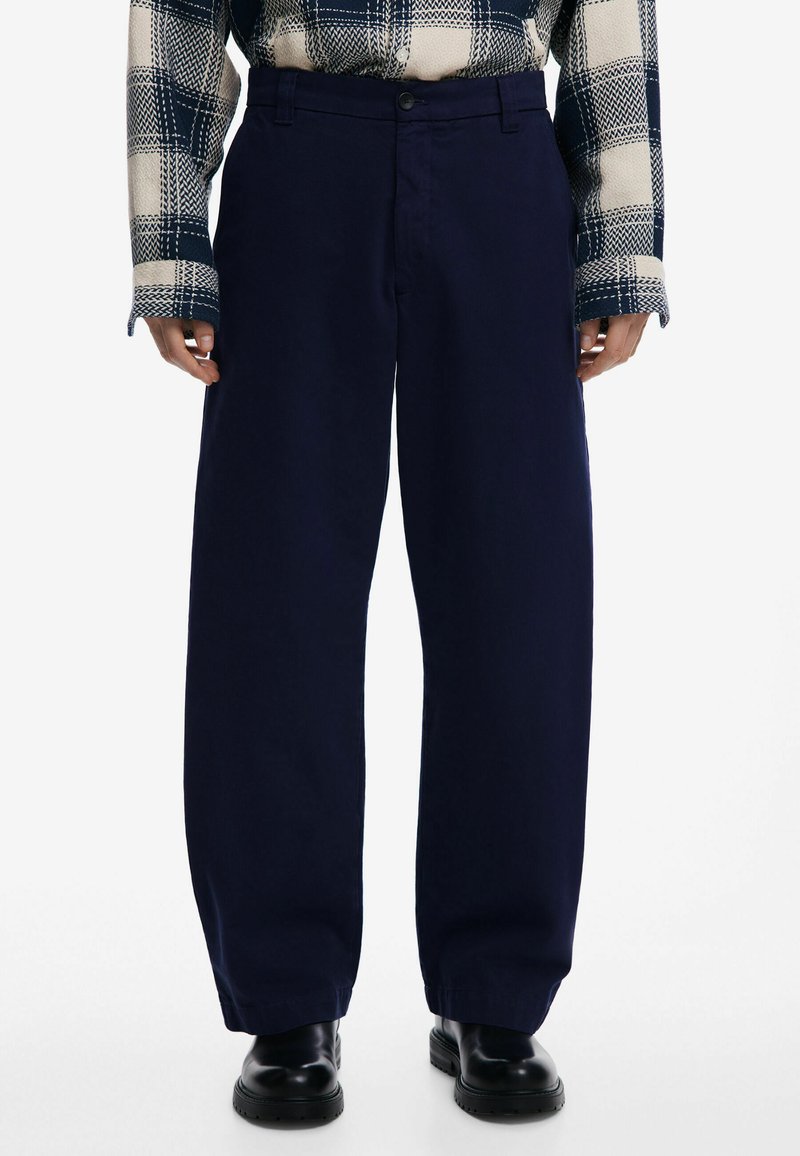 Námornícky modré nohavice s širokými nohavicami a hladkou textúrou, so zapínaním na gombík vpredu a bočnými vreckami, skombinované s károvanou košeľou.