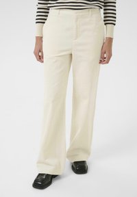 Crème-kleurige ribfluwelen broeken met een recht model en een getextureerde stof, gecombineerd met zwarte chunky schoenen. Verticale ribbelpatroon zichtbaar.