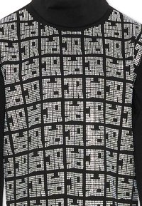 Maglione a collo alto nero decorato con strass argentati disposti in un motivo a griglia, creando una superficie testurizzata e riflettente.