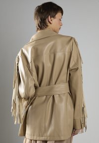Beige Lederjacke mit Fransendetails an den Ärmeln, tailliertem Bund und weicher, glatter Textur. Verfügt über einen klassischen Kragen und eine maßgeschneiderte Passform.