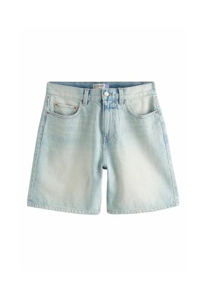 Person trägt hellblaue Jeans-Kniebund-Shorts und ein weißes Top und hebt dieses leicht an, um den Taillenbereich zu zeigen.