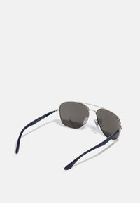 Occhiali da sole aviator in metallo argentato con lenti grigio scuro, astine blu navy e naselli trasparenti. Presentano un design geometrico minimalista.