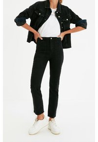 Chaqueta de mezclilla negra con botones plateados, combinada con jeans negros de tiro alto. El modelo lleva una camiseta blanca y zapatillas blancas.