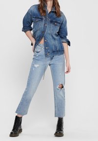 Denim jacket in dark wash with two chest pockets, paired with light wash distressed jeans featuring a large knee tear and cuffed hems.