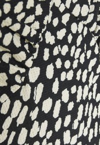 Svart tyg med en texturerad yta som har ett vitt abstrakt djurprintmönster, kännetecknat av olika oregelbundna former och storlekar.