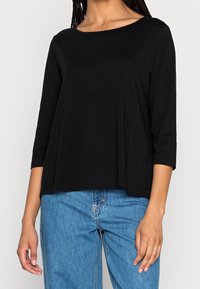 Sort, langærmet bluse med bred halsudskæring og løs pasform, lavet af blødt stof. Dertil let blå denim jeans.