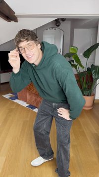 Groene hoodie, grijze denim broek en witte sneakers. Gekenmerkt door een casual ontwerp, een relaxte fit en eenvoudige hardware. Binnenomgeving met planten.