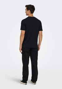 Μαύρο T-shirt με κοντά μανίκια και κλασικό στρογγυλό λαιμό, σε συνδυασμό με μαύρο cargo παντελόνι. Το ύφασμα φαίνεται μαλακό με άνετη εφαρμογή.