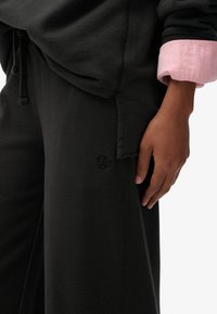 Sorte joggingbukser med en blød struktur og elastisk taljebånd, med en ton-i-ton logo og en kontrasterende pink manchet på en sweatshirt.