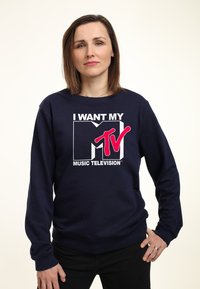 Marinblå sweatshirt med en djärv grafisk design som visar "JAG VILL HA MITT MTV" i vit och rosa text. Långa ärmar, rund hals och avslappnad passform.
